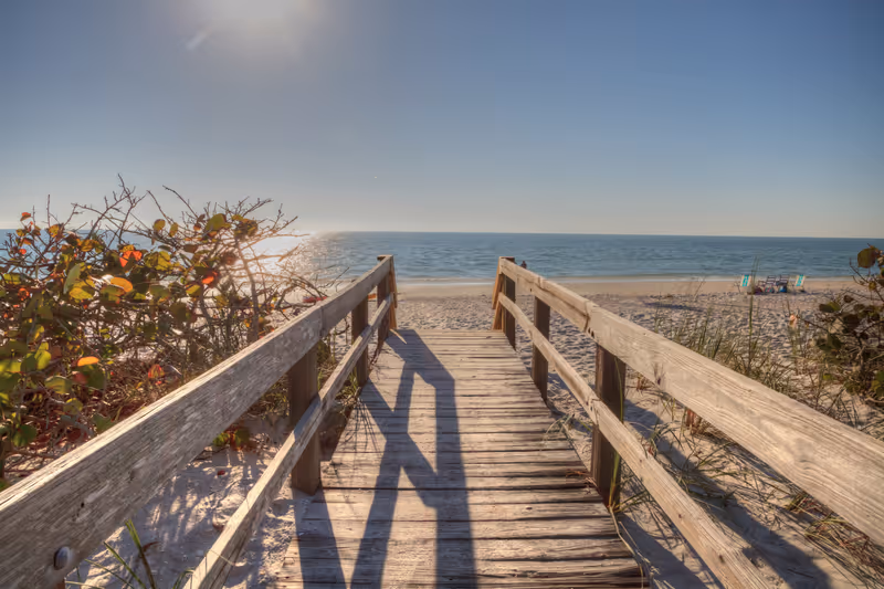 Boardwalk across the white sand beach of Delnor-Wiggins Pass State Park with a blue sky above in Naples, Florida.
