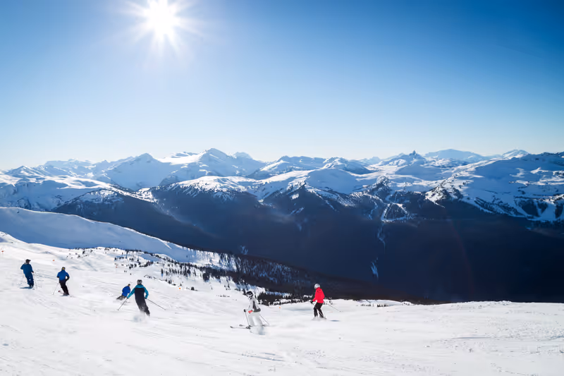 Skiers on a hill at the top of Blackcomb, 7th Heaven, with a view looking toward Whistler on a sunny day.