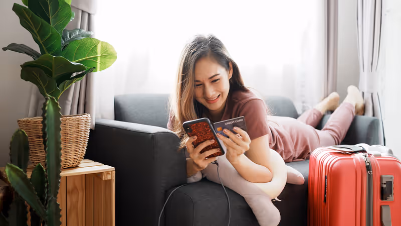 Attractive Asian woman with travel baggage have using smartphone booking flight tickets in online website and Purchase, Pay by credit card. Woman success booking travel tickets in promotion time.