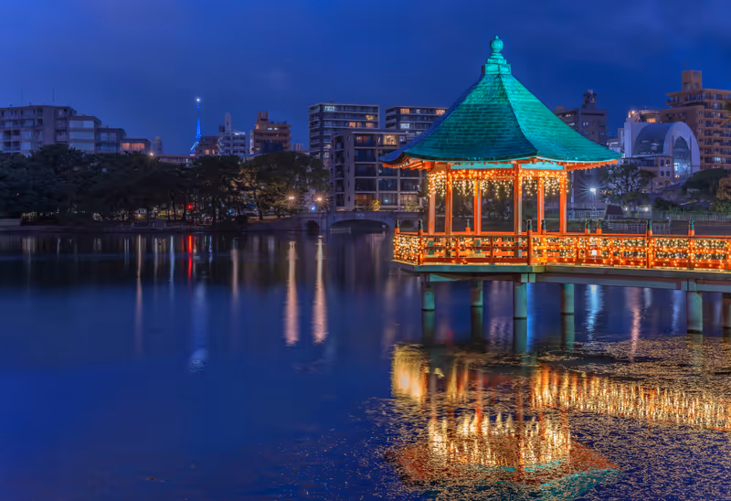 fukuoka, kyushu - december 06 2021: Night view of the Ukimi-do Pavilion light-up with luminous garlands reflecting in the pond of the Ohori Park with the needle of Fukuoka tower in background.