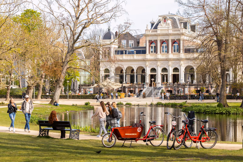 Amsterdam, Netherlands, April 18, 2022; Tourists walk and cycle in the famous Vondelpark with the Vondelpark Pavilion in the background, built by architect W. Hamer in Italian Renaissance style.