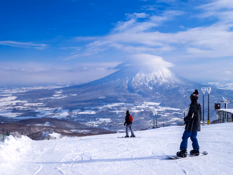 Snowboarder and skier looking at snowy volcano with cap cloud (Niseko, Hokkaido, Japan)