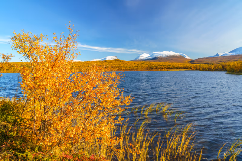 Njakajaure with Lapporten in background in september with autumn colors and snow on the mountain, Abisko national park, Swedish Lapland, Sweden