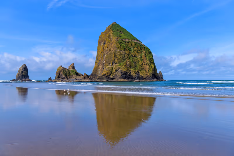 Haystack Rock - A sunny Spring morning view of famous Haystack Rock reflecting on smooth sandy Cannon Beach. Oregon, USA.