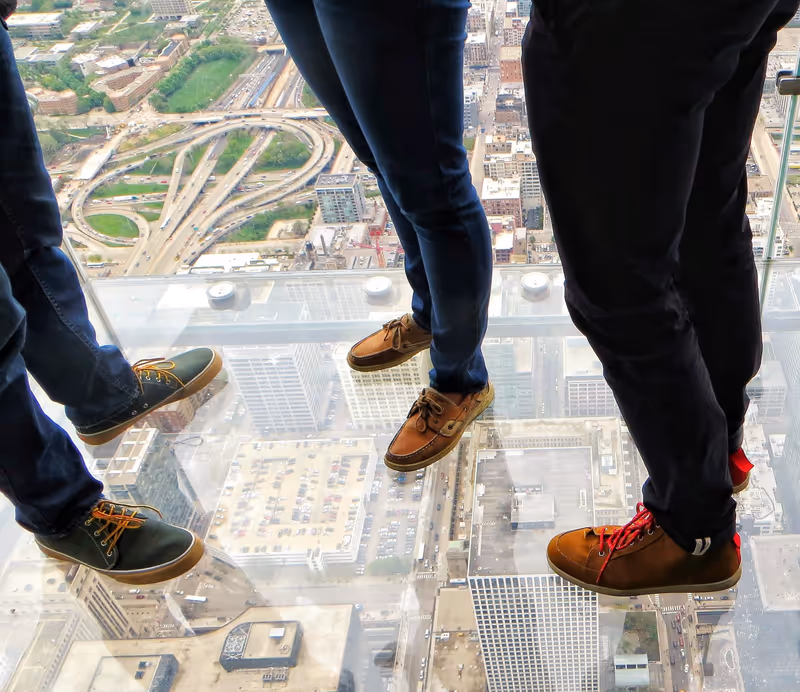 Three brave people on the glass platform on the skydeck of the tower in Chicago, which gives the sensation of flying in the city view