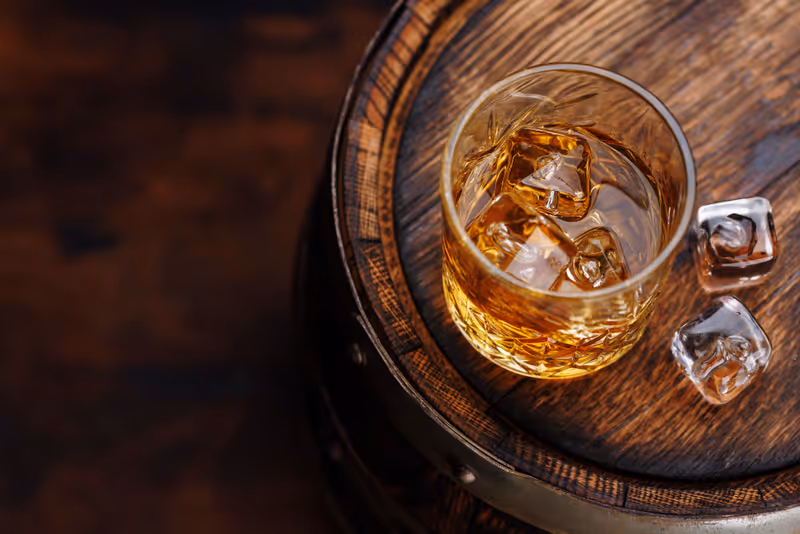 Whiskey glass with ice on a rustic barrel, a classic sip. With copy space