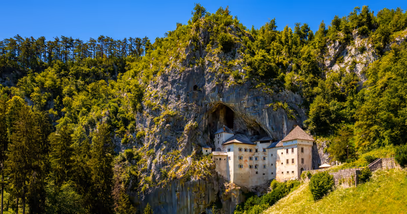 Panorama of Predjama castle built in a cave in Slovenia. Popular tourist attraction and historic monument in an idyllic valley near Postojna Caves on a summer day. Wide angle scenery and major sight.