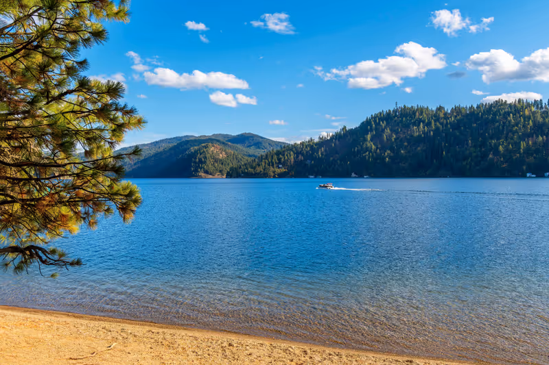 A boat passes in front of a small sandy beach at Beacon Point, a stop on the Centennial Trail, on lake Coeur d'Alene's Wolf Lodge Bay, in Coeur d'Alene, Idaho, USA.