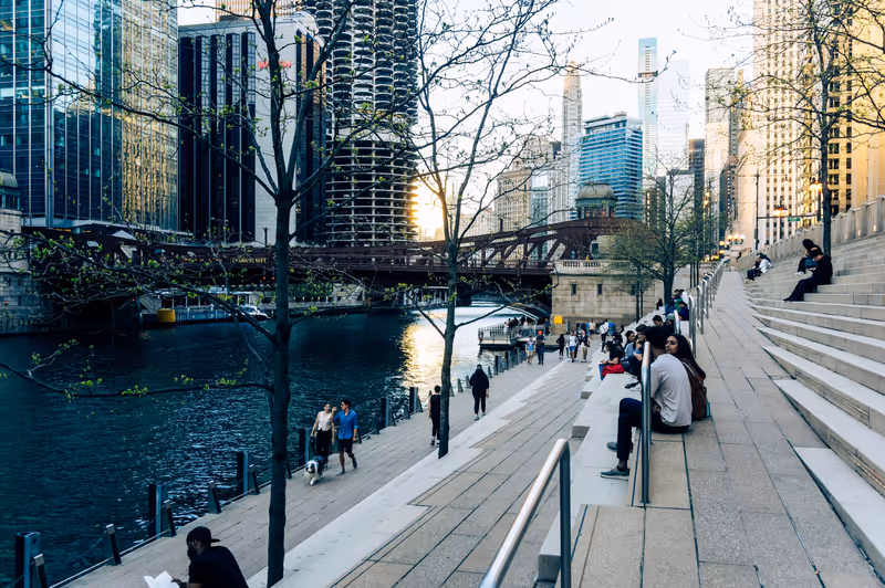 Chicago, IL - April 30 2024: People sitting, relaxing, strolling, reading at the steps next to the Chicago riverwalk with the setting sun reflected on the buildings in the distance