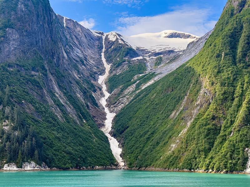 Scenic waterfall, partly frozen, with meltwater from icy mountaintop along Tracy Arm fjord on a sunny morning early in summer in southeast Alaska