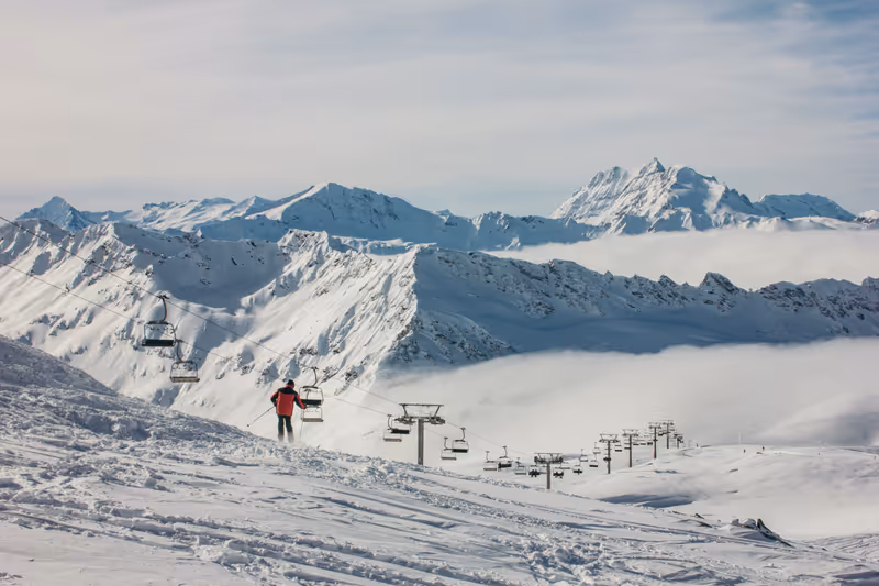 A skier stands near the Cascade chairlift, surrounded by breathtaking snow-covered peaks in Val d'Isère, France