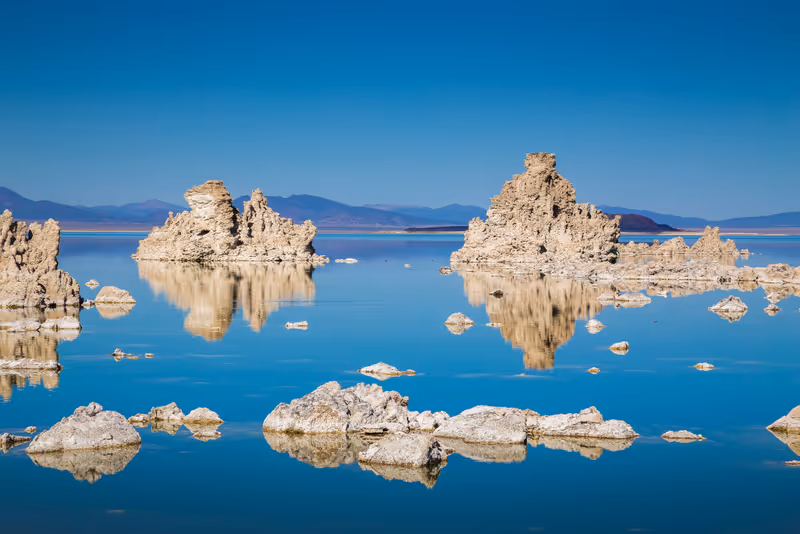 Classic view of fascinating tufa rock formations mirrored on calm water surface of famous Mono Lake on a beautiful sunny day with blue sky in summer, Mono County, California, USA