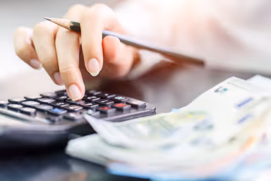 Close up right hand female using calculator in Euro banknotes background. Calculation at home